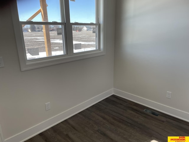 empty room featuring dark wood-style flooring, visible vents, and baseboards