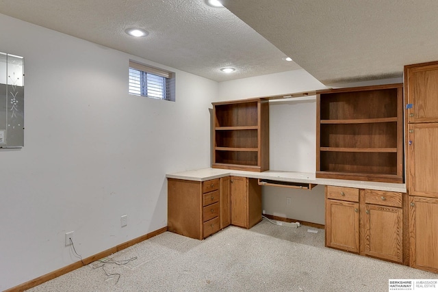 unfurnished office featuring built in desk, light colored carpet, a textured ceiling, and baseboards