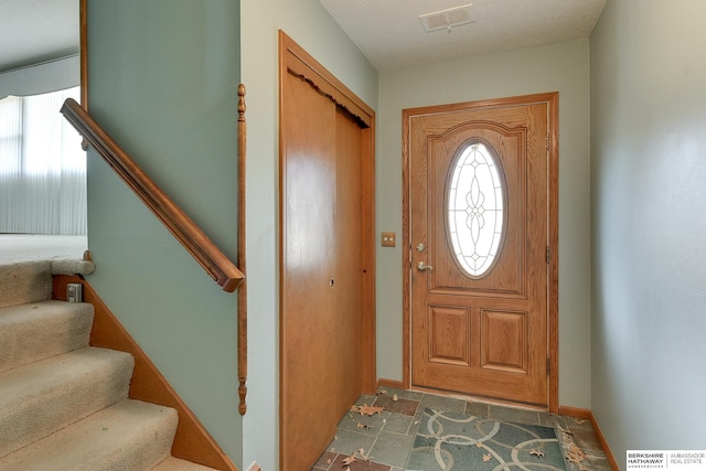 foyer entrance featuring stairway, stone finish floor, baseboards, and visible vents