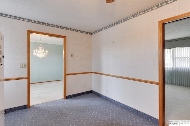 empty room with ornamental molding, carpet floors, an inviting chandelier, wallpapered walls, and baseboards