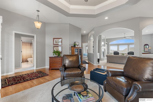 living room with a tray ceiling, ornamental molding, ceiling fan, light wood-type flooring, and baseboards