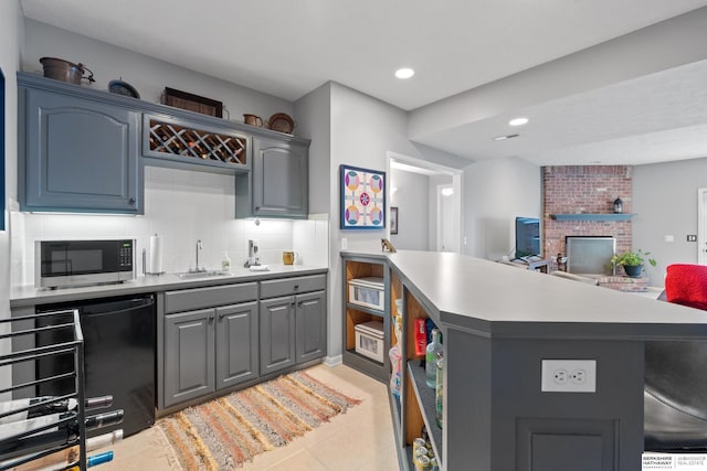 kitchen featuring tasteful backsplash, stainless steel microwave, a peninsula, gray cabinets, and a sink