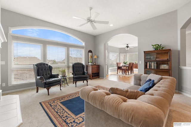 living area with arched walkways, ceiling fan, a wealth of natural light, and light colored carpet