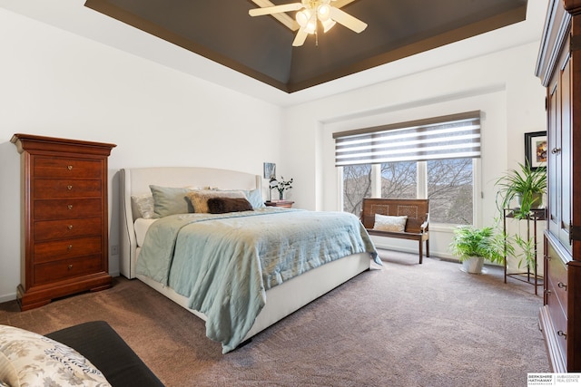 carpeted bedroom featuring a tray ceiling and a ceiling fan