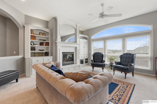 living room with a ceiling fan, baseboards, light carpet, and a tiled fireplace