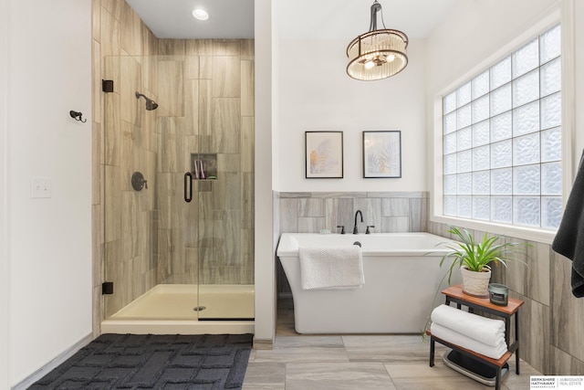 bathroom featuring a stall shower, tile walls, and a soaking tub