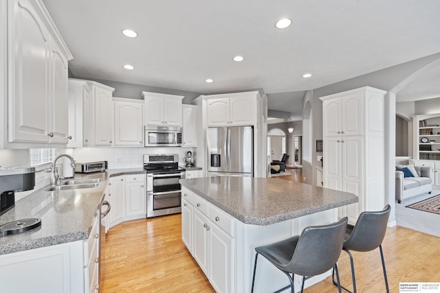 kitchen featuring a kitchen bar, appliances with stainless steel finishes, arched walkways, and a sink