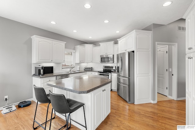 kitchen with appliances with stainless steel finishes, a breakfast bar, visible vents, and white cabinetry