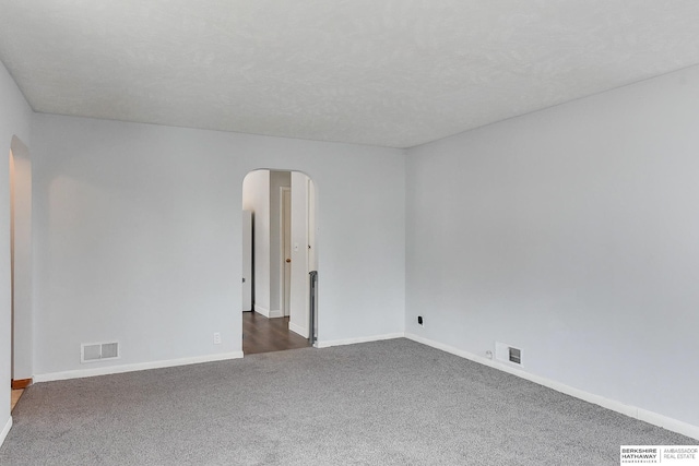 spare room with arched walkways, dark carpet, visible vents, and baseboards