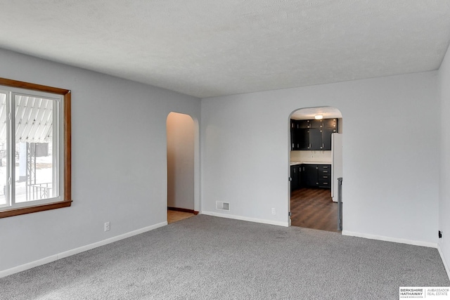 carpeted empty room with arched walkways, visible vents, a textured ceiling, and baseboards