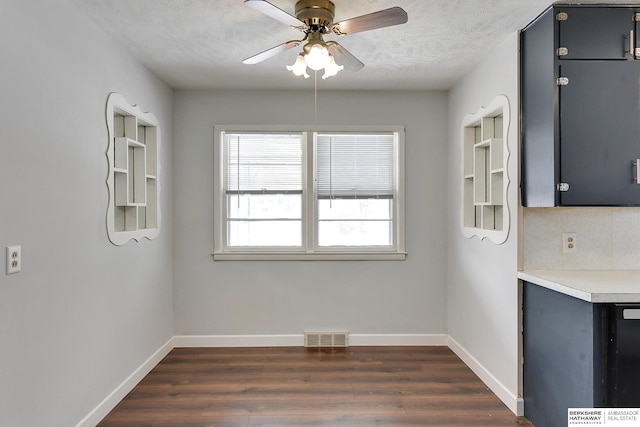 unfurnished dining area featuring dark wood-type flooring, visible vents, a textured ceiling, and baseboards