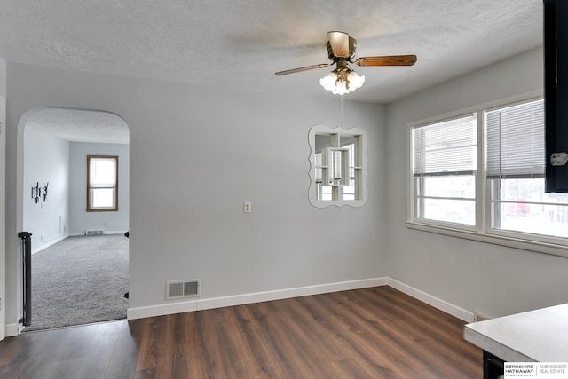 unfurnished dining area featuring arched walkways, a textured ceiling, visible vents, baseboards, and dark wood-style floors