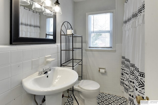 bathroom featuring toilet, a wainscoted wall, tile walls, and a wealth of natural light