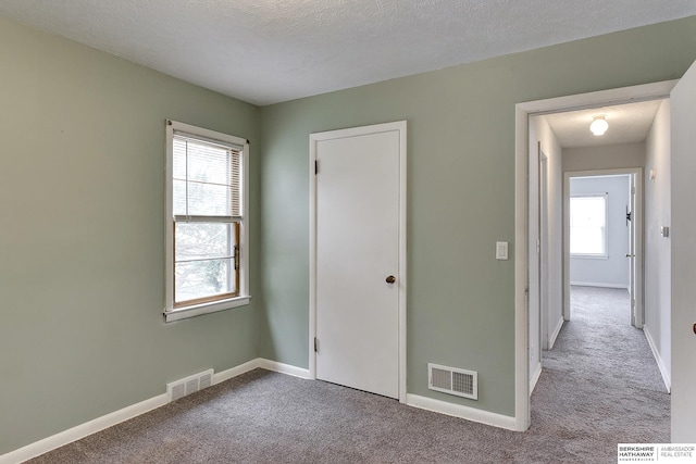 unfurnished bedroom featuring carpet floors, multiple windows, and visible vents