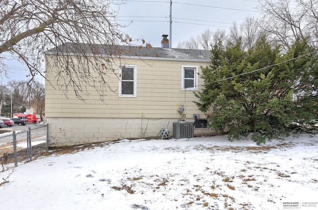 view of snowy exterior with a chimney, cooling unit, and fence