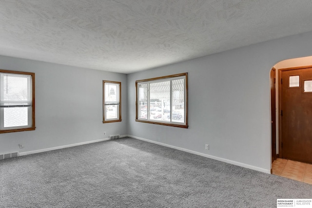 empty room featuring baseboards, visible vents, arched walkways, a textured ceiling, and carpet floors