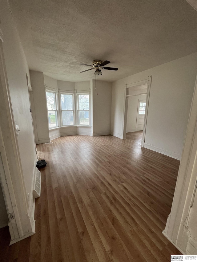 unfurnished room with a textured ceiling, ceiling fan, baseboards, and light wood-style floors