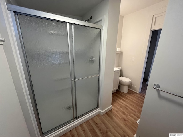 bathroom featuring a shower stall, toilet, and wood finished floors