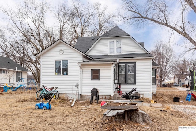 rear view of property with a shingled roof and a playground