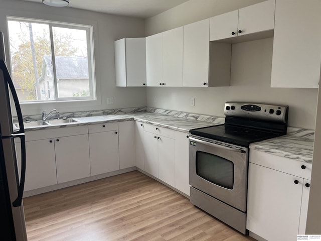 kitchen with light wood finished floors, stainless steel electric stove, freestanding refrigerator, white cabinetry, and a sink