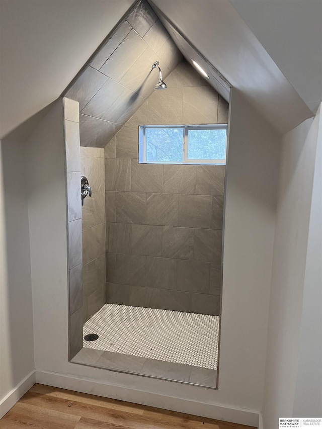 full bathroom featuring tiled shower, vaulted ceiling, and wood finished floors