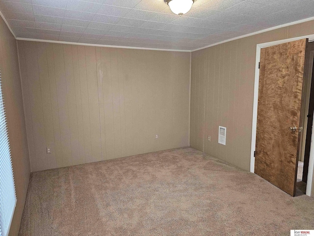 carpeted spare room with visible vents, wood walls, and crown molding