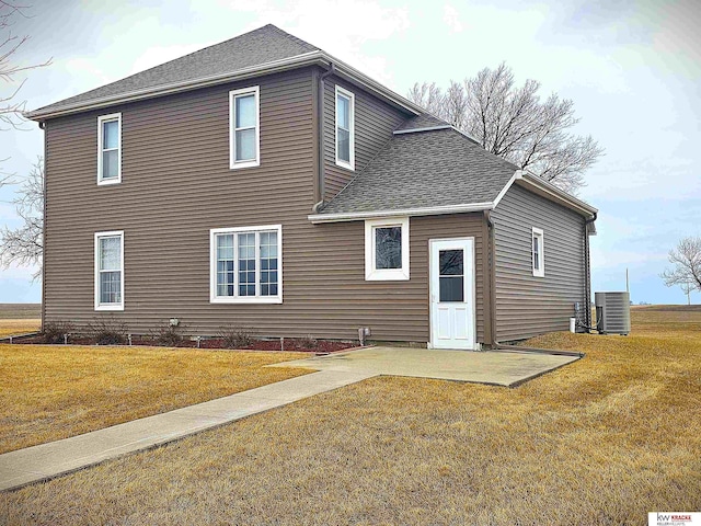 rear view of house featuring a yard, central AC, and a shingled roof