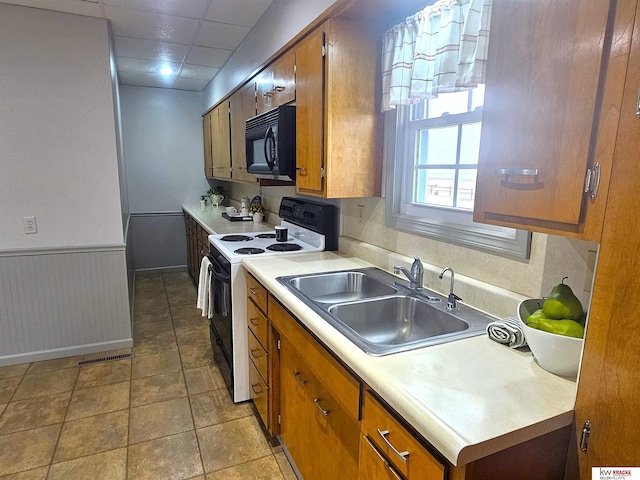 kitchen featuring a sink, light countertops, electric stove, black microwave, and wainscoting