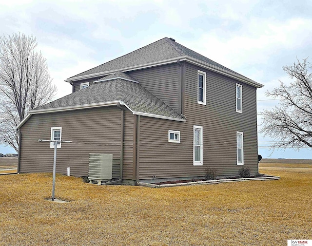 view of home's exterior with cooling unit, a lawn, and roof with shingles