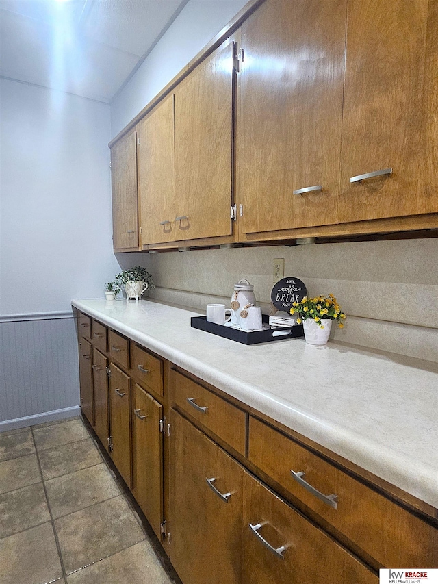 kitchen with a wainscoted wall, brown cabinets, and light countertops