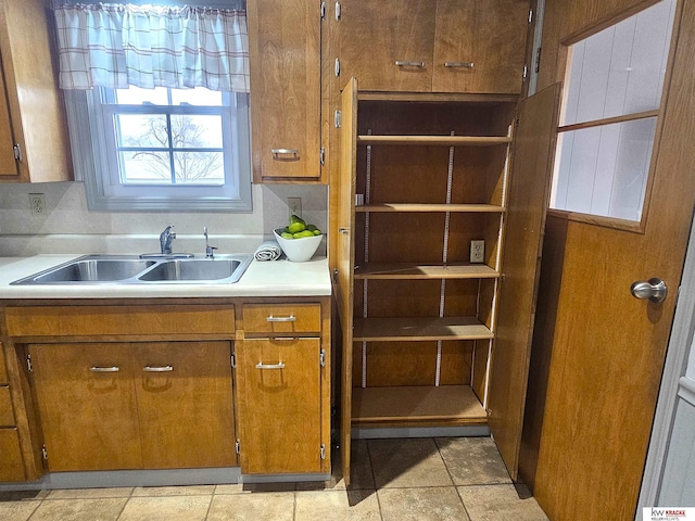 kitchen featuring a sink, brown cabinets, light tile patterned flooring, and light countertops