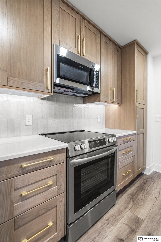 kitchen with stainless steel appliances, tasteful backsplash, wood finished floors, and light countertops