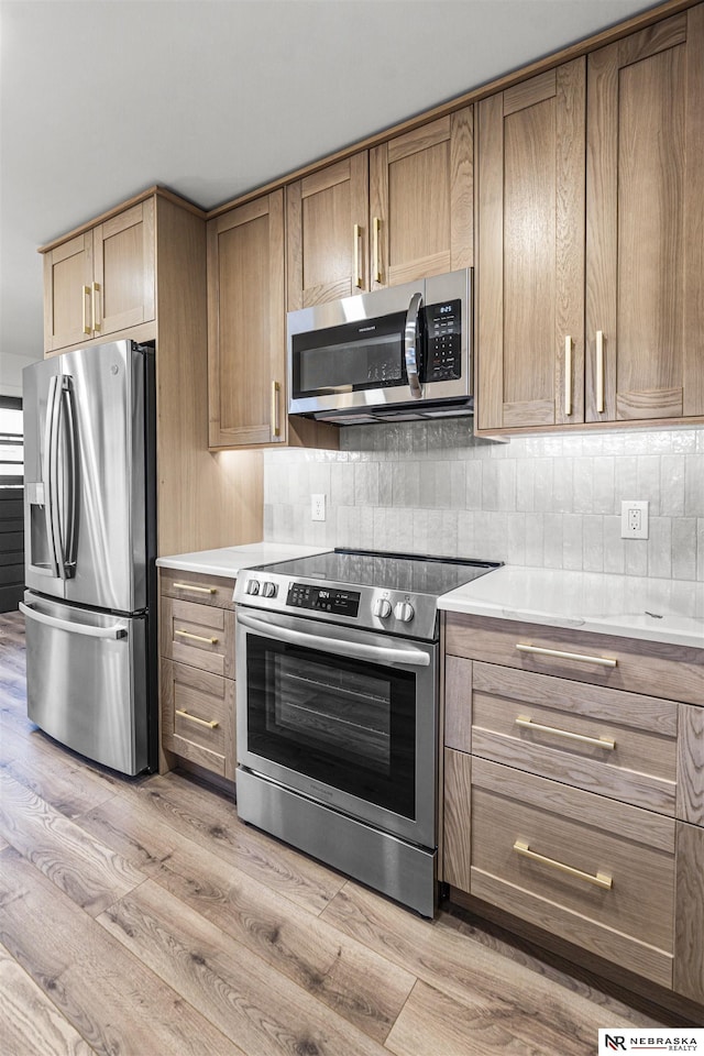 kitchen featuring light countertops, decorative backsplash, appliances with stainless steel finishes, brown cabinetry, and light wood-style floors