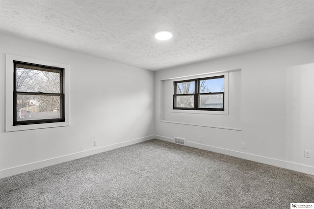 carpeted spare room with a wealth of natural light, visible vents, a textured ceiling, and baseboards