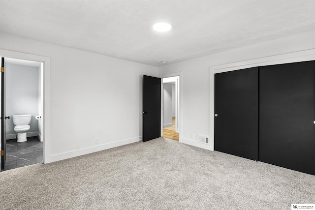 unfurnished bedroom with ensuite bathroom, a closet, carpet, and visible vents