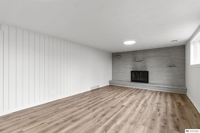 unfurnished living room featuring a brick fireplace, visible vents, and light wood finished floors