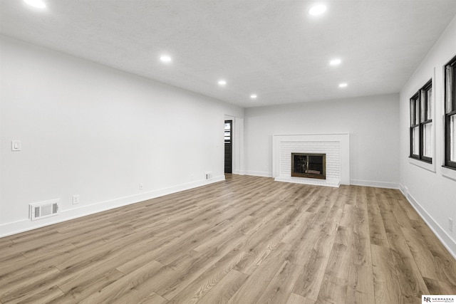 unfurnished living room with light wood-style flooring, recessed lighting, visible vents, a brick fireplace, and a wealth of natural light