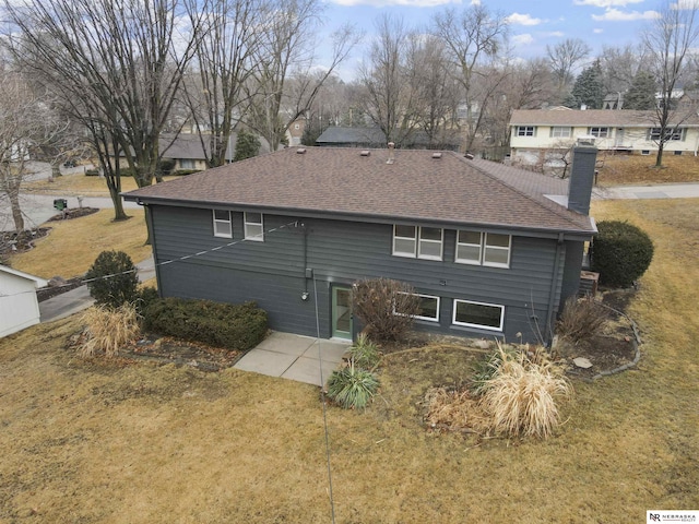 back of house with a shingled roof, a chimney, and a lawn