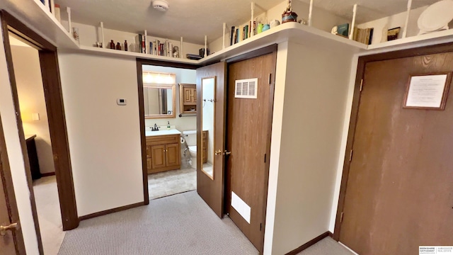 hall with light carpet, baseboards, visible vents, and a sink