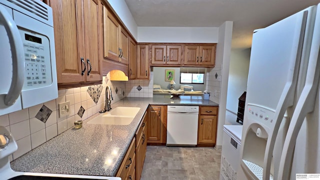 kitchen featuring white appliances, decorative backsplash, a sink, and brown cabinets