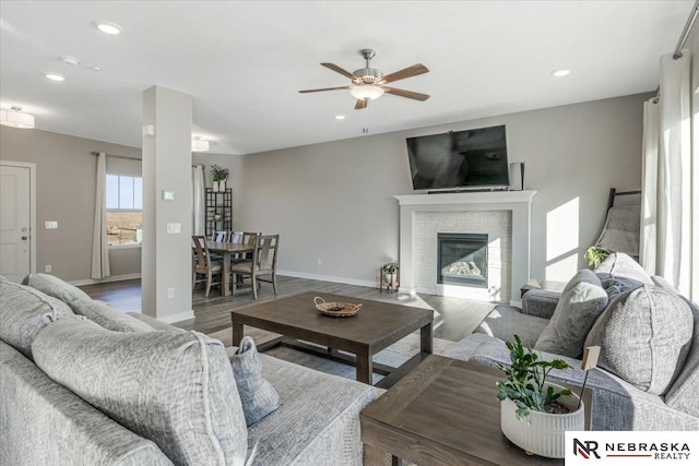 living room featuring recessed lighting, wood finished floors, a ceiling fan, baseboards, and a glass covered fireplace