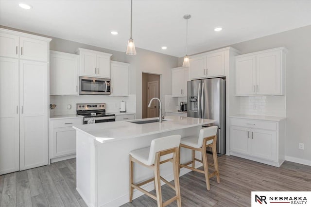 kitchen with a kitchen island with sink, appliances with stainless steel finishes, white cabinets, and a sink