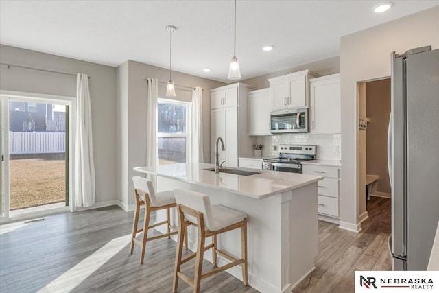 kitchen with stainless steel appliances, a sink, white cabinets, light wood-style floors, and backsplash