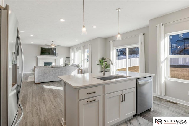 kitchen with light wood finished floors, visible vents, appliances with stainless steel finishes, a fireplace, and a sink