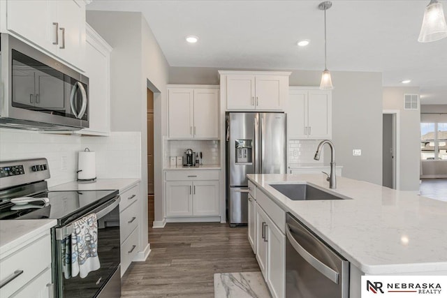 kitchen with an island with sink, hanging light fixtures, stainless steel appliances, white cabinetry, and a sink