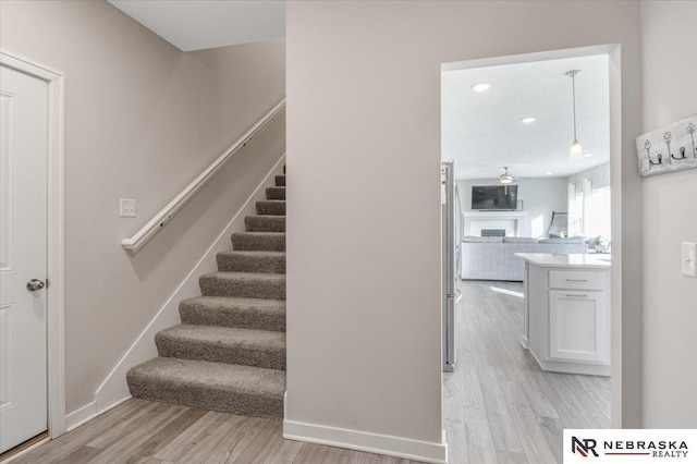 staircase featuring a fireplace, wood finished floors, and baseboards