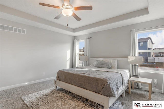 carpeted bedroom with a raised ceiling, visible vents, and multiple windows