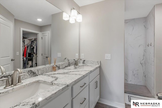 full bath featuring a tile shower, double vanity, a sink, and a walk in closet