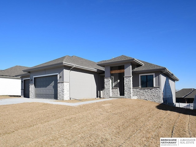 prairie-style house featuring a garage, stone siding, driveway, and a shingled roof