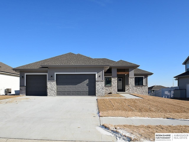 prairie-style house featuring an attached garage, stone siding, central AC, and concrete driveway